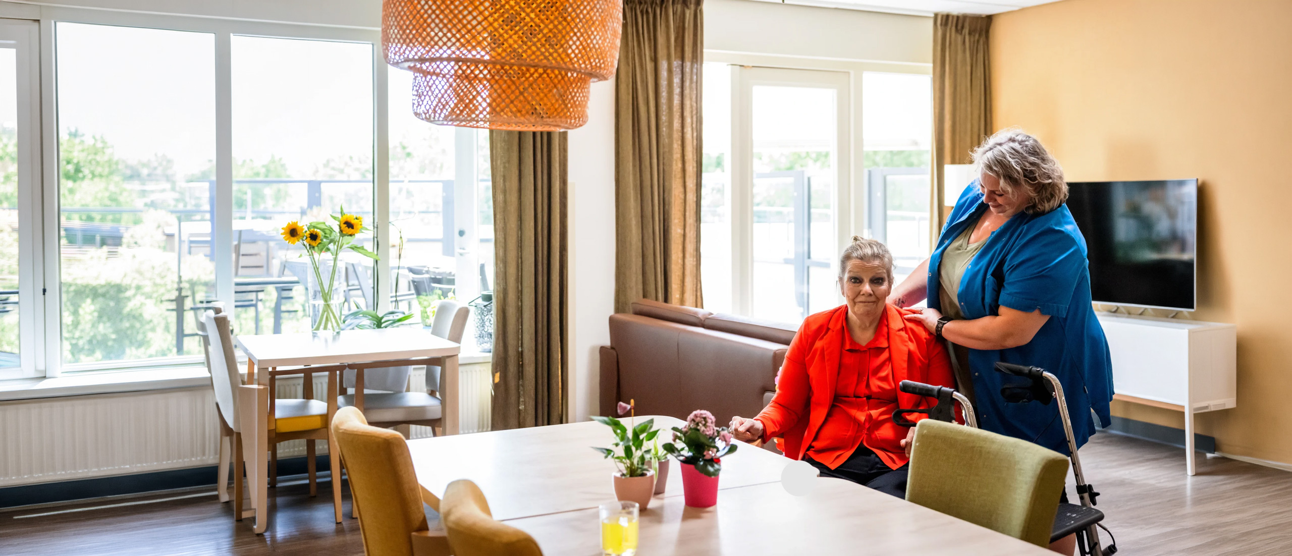 Zorgcollega van Topaz staat naast een bewoner aan tafel
